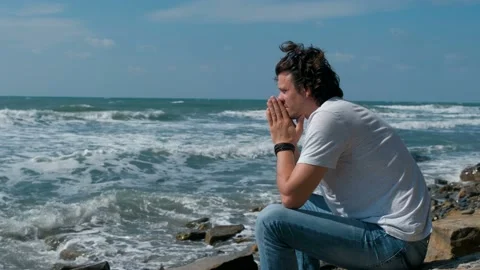 Upset young man sitting on the beach and looking at waves. Stock Footage 116022817