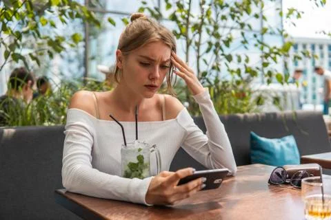 Upset young student watching broadcasting online on modern mobile phone. Blond Stock Photos