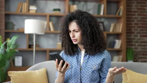 Upset young woman rejected while talking on mobile phone while sitting on sofa  Stock Footage 320414660