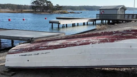 Upside down boat resting on sandy shore near calm sea with wooden pier Stock Footage 331891653