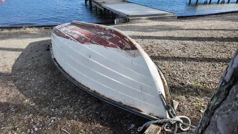 Upside down boat resting on sandy shore near calm sea with wooden pier. Stock Photos