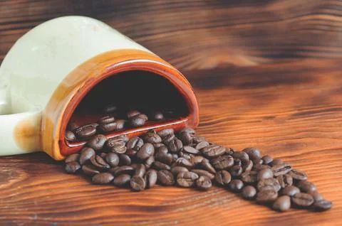 An upside down cup with coffee beans. Coffee beans scattered on a wooden ta.. Stock Photos