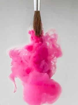 The upside down paintbrush releases clouds of pink acrylic paint isolated on Stock Photos
