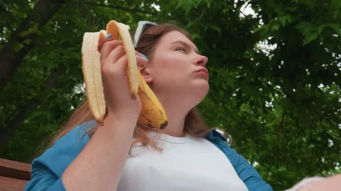 Upward Angle View of Lady Eating Plantain Outdoors Under Green Trees Stock Footage 328359997