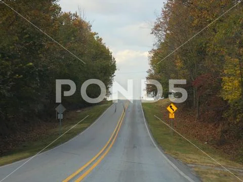 Upward sloping road with speed limit signs and colorful trees on both ...