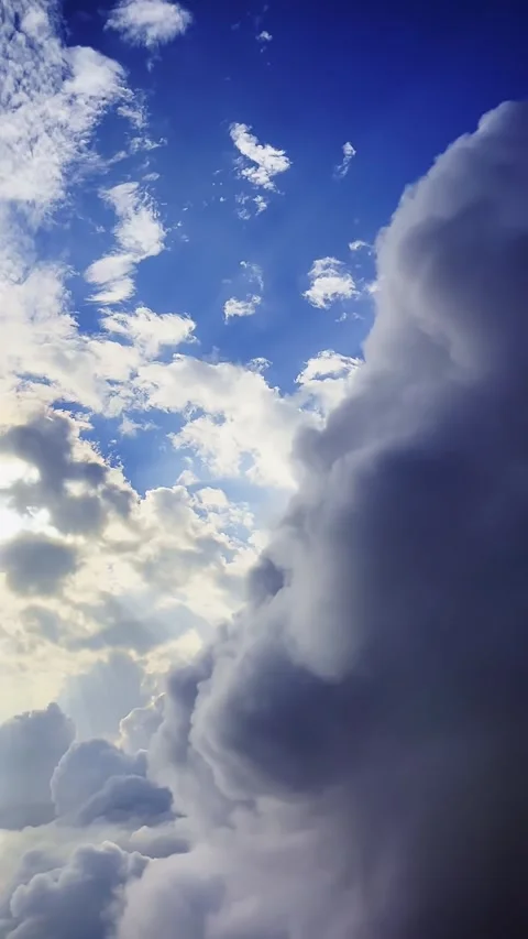 Upward view of glowing sun behind layered clouds over deep blue sky with soft Stock Footage 345835688