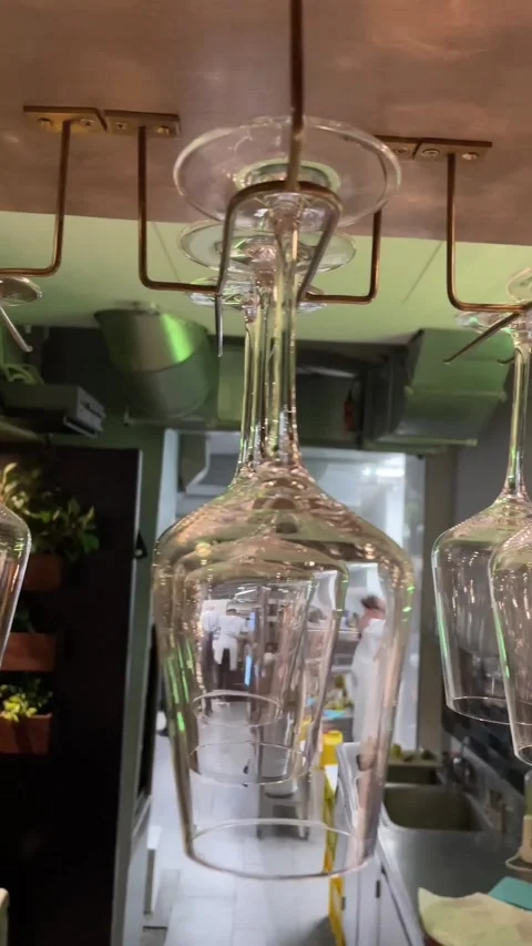 Upward view of inverted wine glasses hanging from metal rack above restaurant Stock Footage 344584437