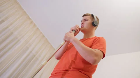 Upward View Of Man Singing Into Mop Handle With Headphones Stock Footage 319916171