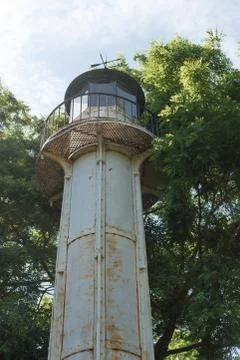 Upward view on old grey painted rusty iron lighthouse tower with high trees and Stock Photos