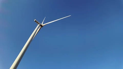 Upward view of a single wind turbine with long blades spinning under a bkue sky Stock-Footage 314817304