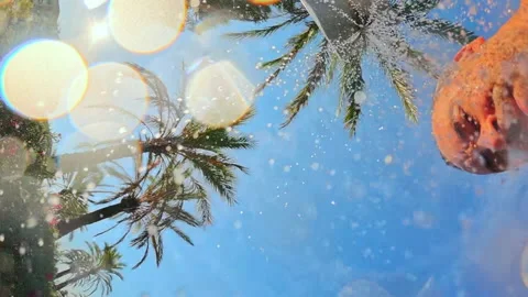 Upward view of water drops falling against a blue sky, palm trees, and blooming Stock Footage 343002843