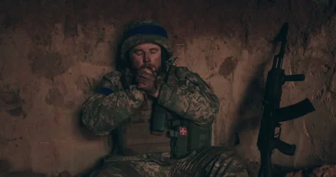 A Urain soldier sits on the bare ground in a dugout with a rosary Stock Footage 261749491