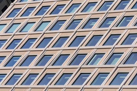 Urban building facade with repeating window patterns in afternoon sky refle.. Stock Photos