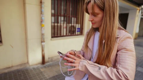 Urban clad blonde checking smartphone while standing on city street Video stock 308352139