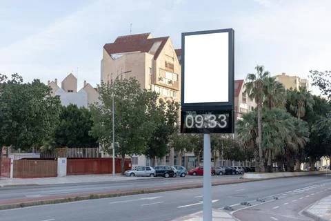 Urban digital clock post with a blank advertising panel against a cityscape Stock Photos