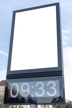 Urban digital clock post with a blank advertising panel against a cityscape Stock Photos