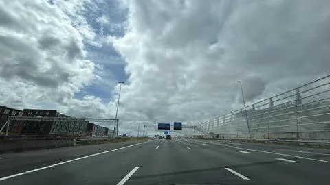 Urban highway under dramatic cloudscape with sound barrier and traffic signage Fotos Stock