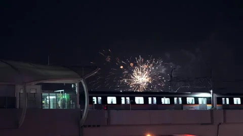 Urban light rail train leaving station with fireworks in the night sky Stock Footage 331768513