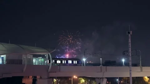 Urban light rail train leaving station with fireworks in the night sky Stock Footage 331768517