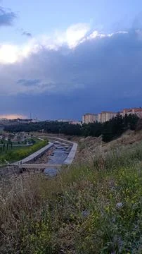 Urban River Park with Dramatic Clouds and City Buildings Stock Photos