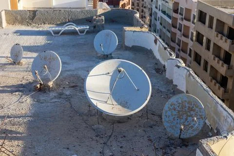 An urban rooftop scene featuring multiple satellite dishes against a sunset b Stockfoto's