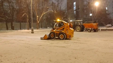 Urban snow removal in progress. Compact loader and tractor clear snowy street Stock Footage 327130845