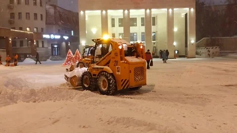 Urban snow removal in progress. Compact loader and tractor clear snowy street Stock Footage 327163255