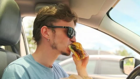 Urban young man eats kebab with meat in bread while sitting driving a car Stock Footage 279395954