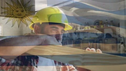 Uruguay flag over site worker carrying wood beam. 動画素材 138718014