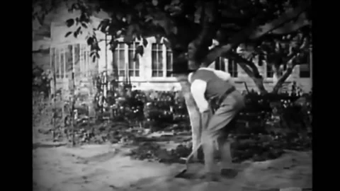 US - 1927 - in this silent comedy, a sheriff digs up soil in his garden, hitting Stock Footage 277299742