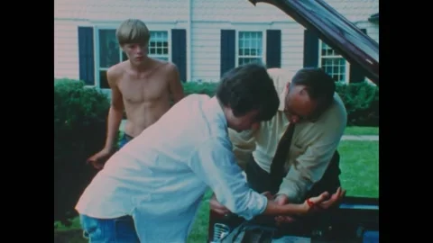 US - 1970 - A man helps a boy who has injured his hand working on a car Vídeos de archivo 328706969