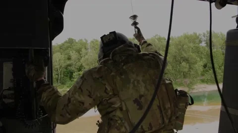 U.S. Air Force airman looking out from helicopter flying over river Stock Footage 213581066
