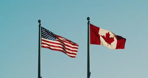U.S.A and Canadian flags flutter in the wind against the sunset sky. Stock Footage 230034507