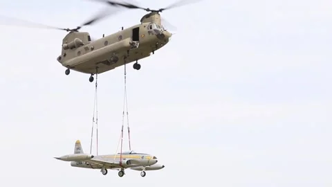 U.S. Army CH-47 Chinook lifting F-80 'Shooting Star' aircraft by sling load Stock Footage 211806360
