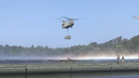 U.S. Army CH-47 Chinook hovering over water with pontoon bridge by sling load Video stock 289628541