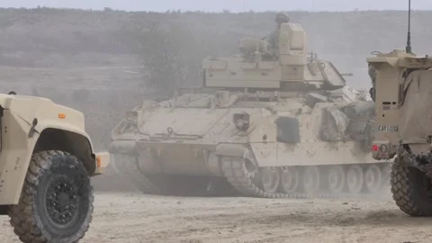 U.S. Army M2A3 Bradley Fighting Vehicle passing Oshkosh JLTV parked on dirt road Stock Footage 301062805