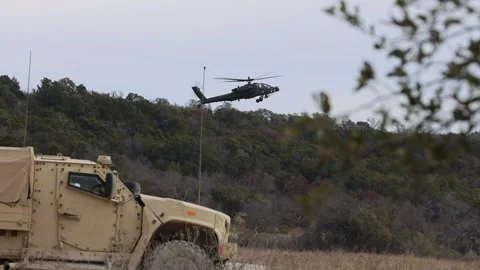 U.S. Army Oshkosh JLTV parked with AH-64 Apache helicopter flying in distance Vídeos de archivo 301062965
