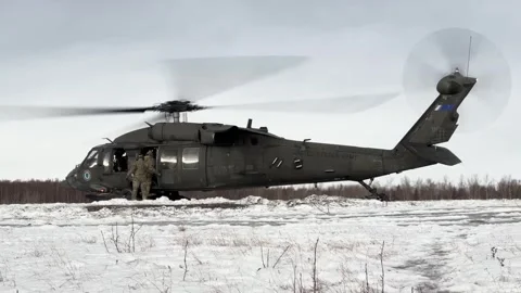 U.S. Army soldier closing door of UH-60 Black Hawk in a snow-covered landscape Stock Footage 295350144