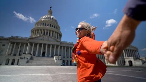 With the US Capitol large in the frame, a blond woman pulls the hand of her Stock Footage 128717738