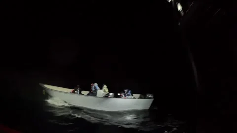 U.S. Coast Guard illuminates illegal aliens aboard intercepted boat with torch Stock Footage 300439826