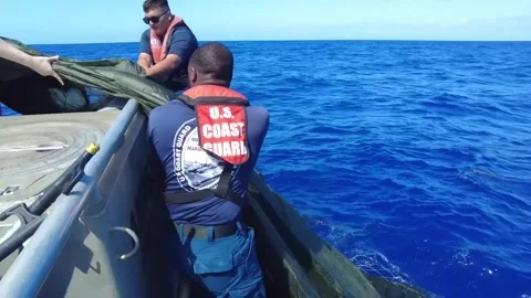 U.S. Coast Guard personnel pulling a parachute out of the ocean onto a boat Stockbeeldmateriaal 295033951