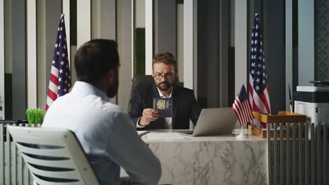 U.S. embassy officer checking U.K. passport and handing document to male visitor Stock Footage 327785230