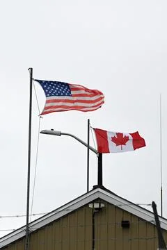 US flag and flag of Canada are waving against the sky and barbed wire. Stock Photos