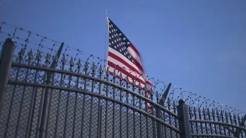 U.S. flag behind barbed wire fencing, detention center or penitentiary Stock Footage 345833327