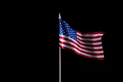 The U.S. flag is developing in the wind against a dark background. Isolate Stockfoto's