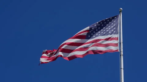 US flag on the flag pole blowing in the wind against deep blue sky Stock Footage 249626244