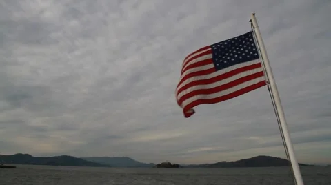 US Flag flying on boat in front of Alcatraz on cloudy day Stock Footage 52855694