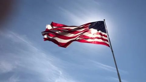 US flag flying in breeze against blue sky Stock Footage 136628596