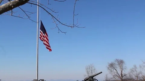 US Flag at Half Mast Waving Against Blue Sky and Historic Artillery Canon Stock Footage 69232187