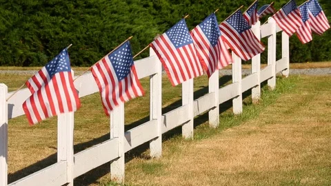 US flags waving on white picket fence. Fourth of July in small town America. Stock Footage 107386880